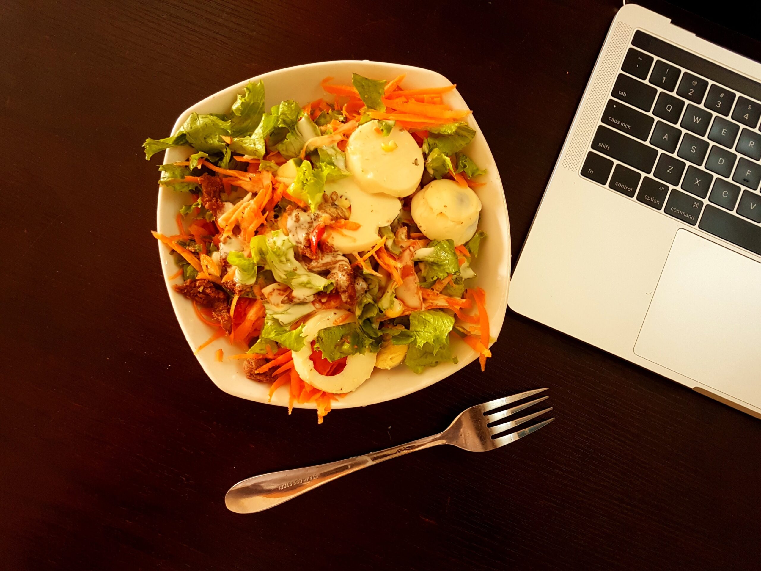 white ceramic bowl with vegetables beside grey laptop computer